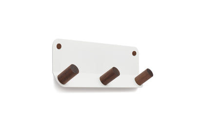 The Plane 3 Wall Hook by Fire Road is a stylish addition to any room, featuring a white, powder-coated steel base and three angled cylindrical wooden pegs.