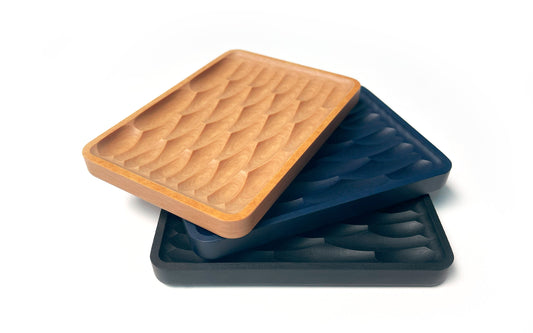 Three rectangular trays with a textured fish scale pattern, stacked slightly askew, featuring light brown, blue, and black colors on a white background. The Fire Road Deco Soap Dish set adds a touch of sustainability to any bathroom decor.