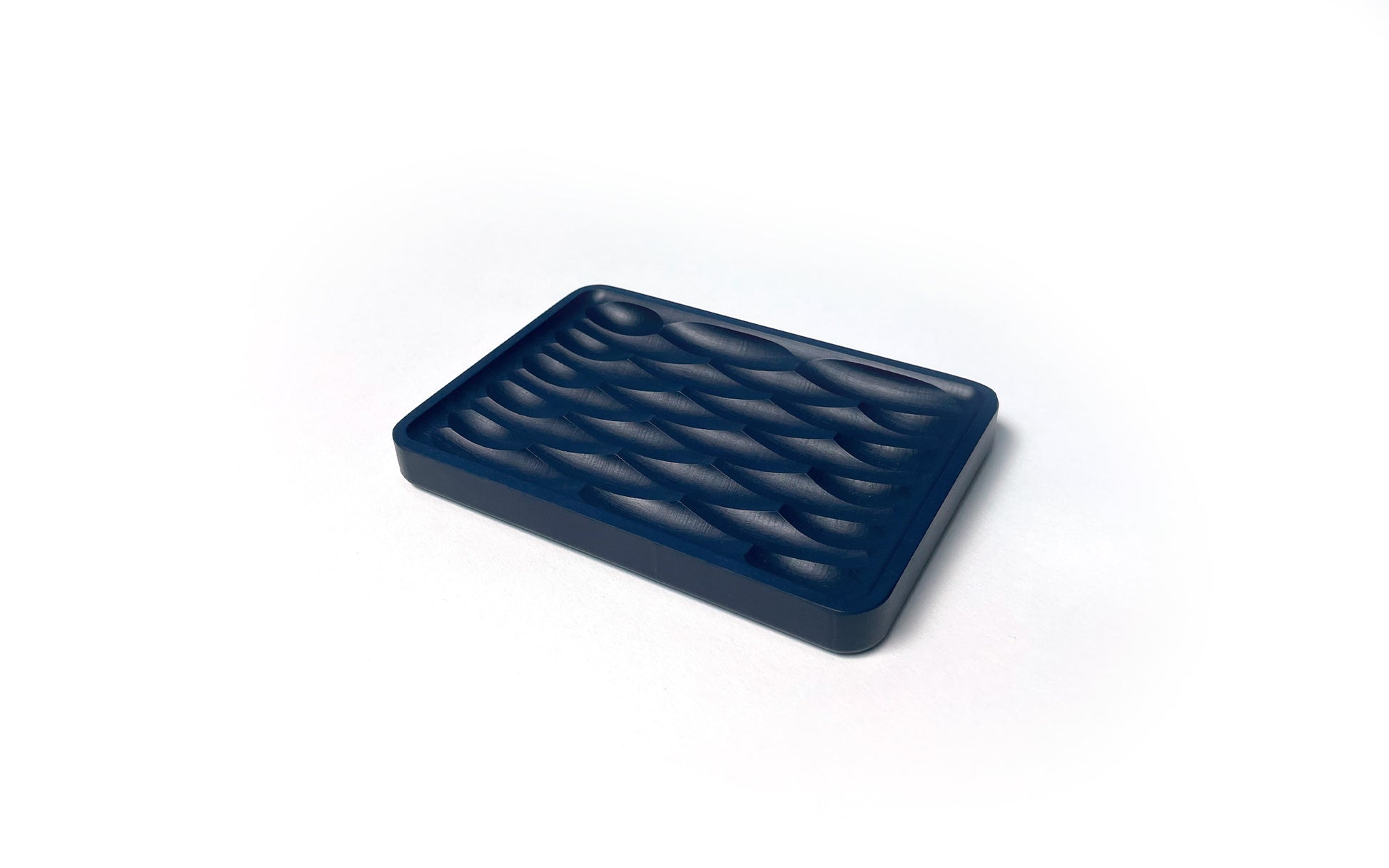 A rectangular object with a textured blue top, possibly an eco-friendly Deco Soap Dish by Fire Road made from recycled paper, against a white background.